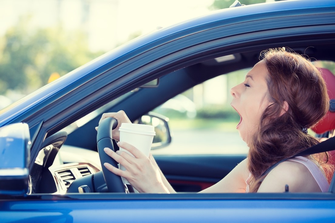 Image of Distract Driving - driving women yawning while holding a coffee cup