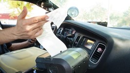 An officer inside a patrol car holding paper printing out of a citation machine.