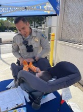 A California Highway Patrol officer helps an infant in a car seat during a car seat fitting event.
