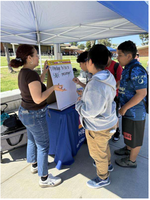 A woman shows students a whiteboard with text at an information booth.